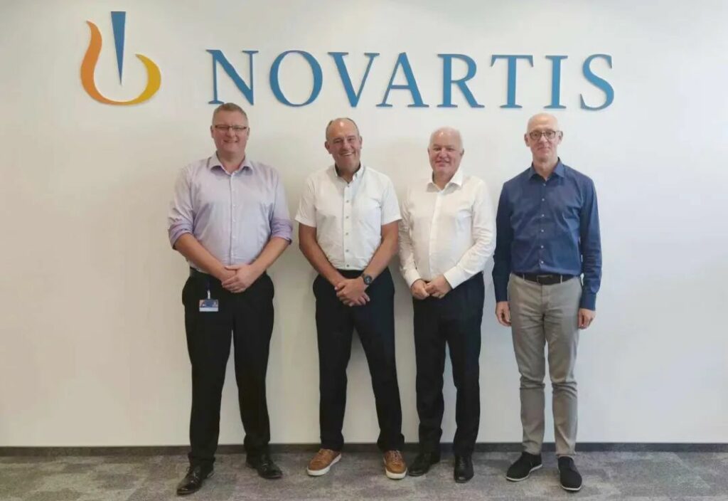 Four men standing in front of a novartis sign.