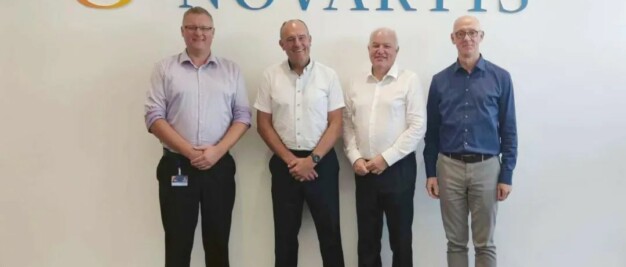 Four men standing in front of a novartis sign.