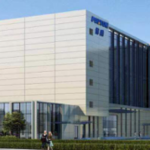 The large modern building at the Porton site boasts glass windows and a fountain in front, set amid lush greenery, showcasing its state-of-the-art construction as a premier drug product GMP facility.