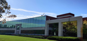 A modern brick and glass building stands proudly with a grassy lawn and trees under a clear blue sky, reminiscent of the purity sought in APIs and chemical intermediates.