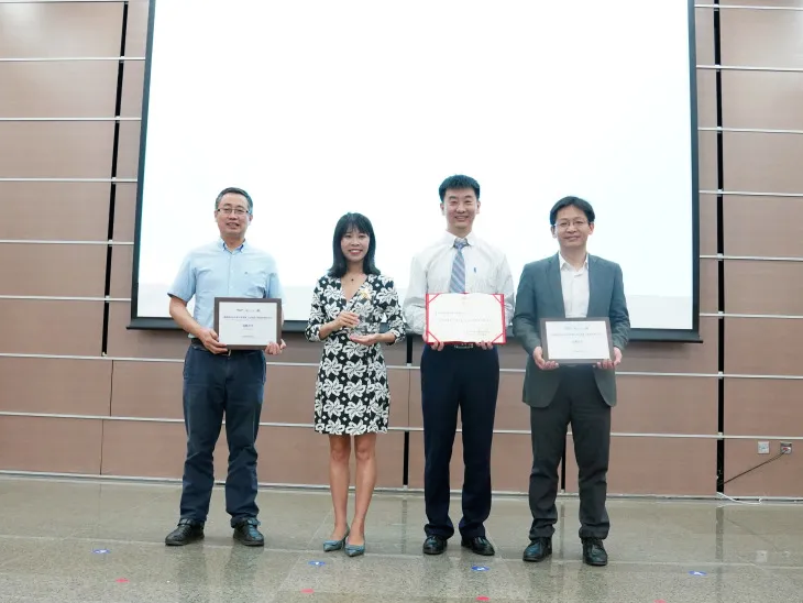 Four people standing in front of a screen holding certificates.