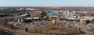 Aerial view of the CfPC's expansive office complex with multiple interconnected buildings, surrounded by parking lots, green spaces, and a pond on a clear day.