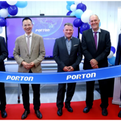 Five men stand behind a ceremonial ribbon labeled "PORTON," with balloons and a screen displaying the same text in the background.