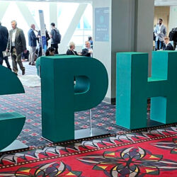 Large green letters spelling "CPHI" are displayed in a carpeted lobby area with people walking and sitting in the background.