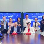 A group of eight people in business attire pose with thumbs up in a conference room, celebrating a strategic partnership. Two are seated at the table, while a screen behind them showcases business logos and text from Porton Pharma Solutions and Shanghai InnoStar.