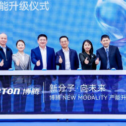 A group of six people in suits stands behind a display table with "PORTON" and Chinese text, giving thumbs up at a company event celebrating the modality capacity upgrade.