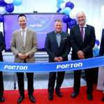 Five men in business attire stand behind a ribbon labeled "PORTON" at an Investment Forum event. Slovenian officials mingle among blue and white balloons in the background.