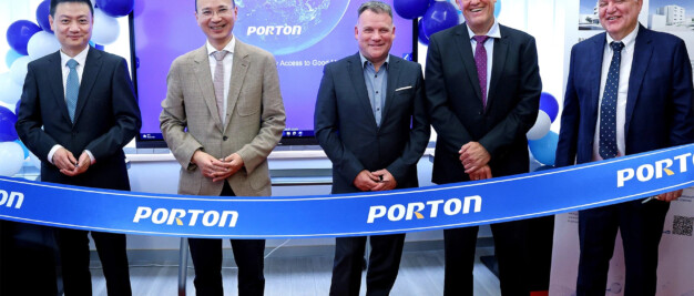 Five men in business attire stand behind a ribbon labeled "PORTON" at an Investment Forum event. Slovenian officials mingle among blue and white balloons in the background.