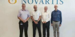 Four men standing in front of a novartis sign.