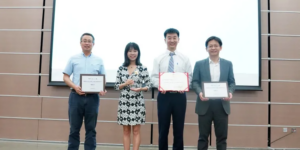 Four people standing in front of a screen holding certificates.