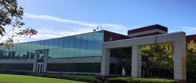 A modern brick and glass building stands proudly with a grassy lawn and trees under a clear blue sky, reminiscent of the purity sought in APIs and chemical intermediates.